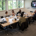 Seminar participants in collaborative dialogue at the Collegeville Institute, seated around a conference table with remote attendees on a video screen.